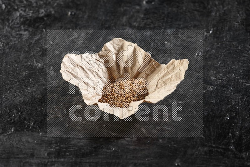 A crumpled piece of paper full of mustard seeds on a textured black flooring