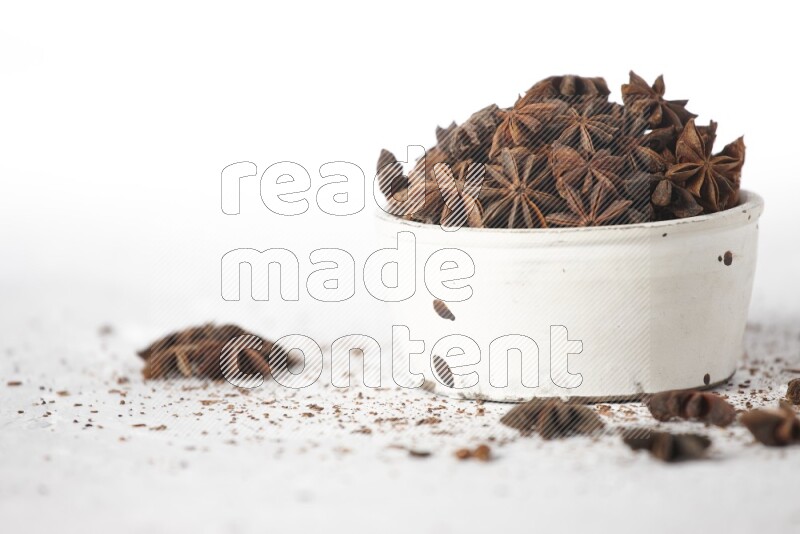 Star Anise in a white bowl and more of it sprinkled on white background