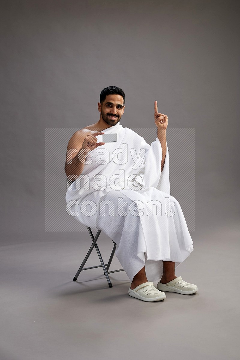 A man wearing Ehram sitting on chair holding ATM card on gray background