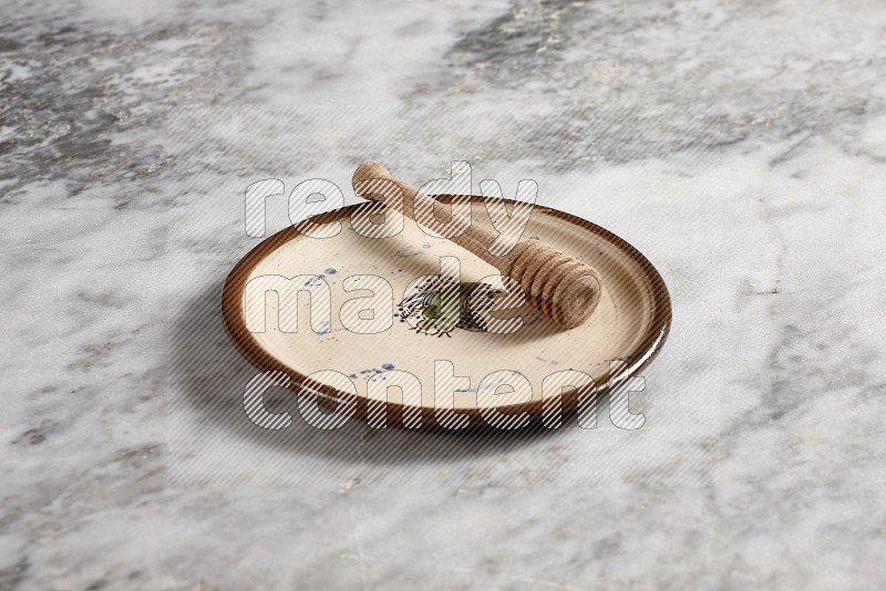 Decorative Pottery Plate with wooden honey handle in it, on grey marble flooring, 45 degree angle