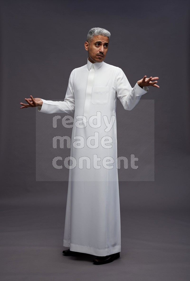 Saudi man wearing thob standing interacting with the camera on gray background