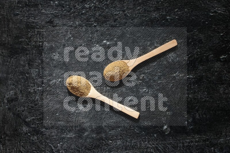 Wooden spoons full of allspice powder on a textured black flooring