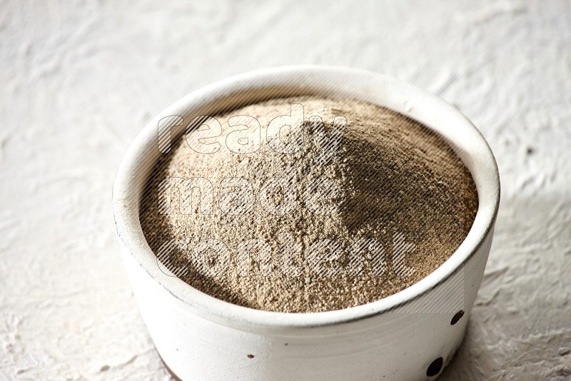 white pottery bowl full of white pepper powder on textured white flooring