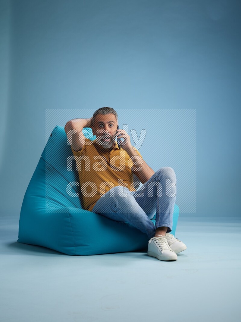 A man sitting on a blue beanbag and talking on the phone