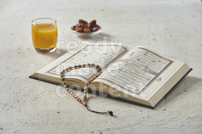 Quran with dates, prayer beads and different drinks all placed on textured white background