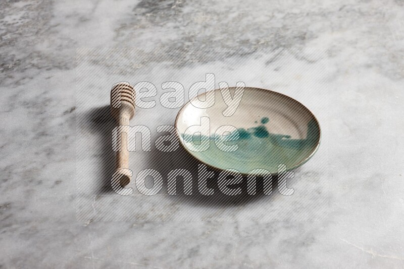 Multicolored pottery plate with wooden honey dipper on the side on grey marble background
