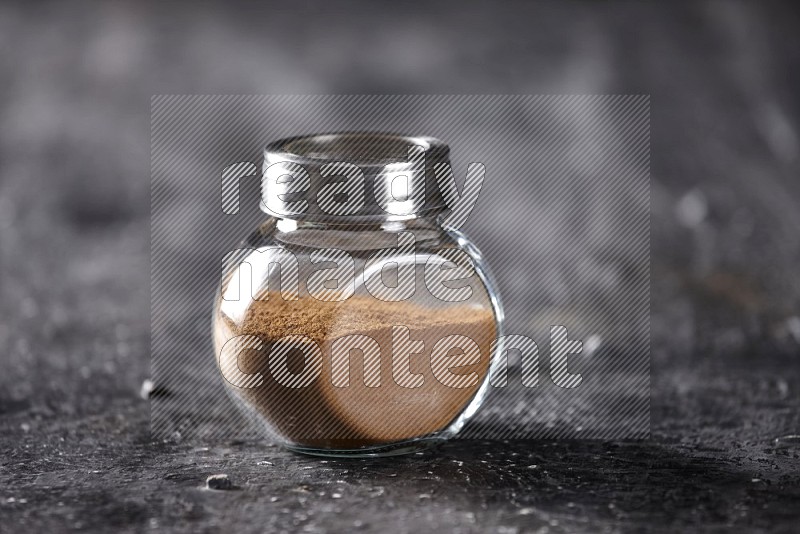 Herbal glass jar full of cinnamon powder on a textured black background