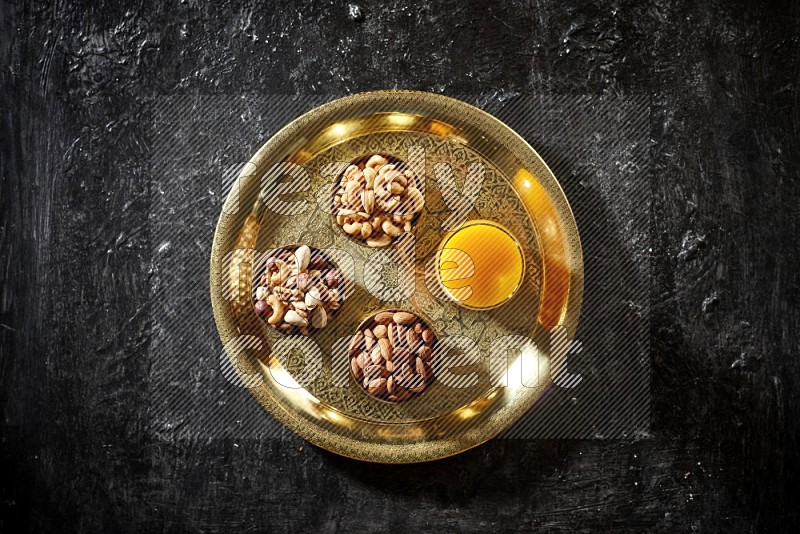 Nuts in metal bowls with qamar eldin on a tray in dark setup