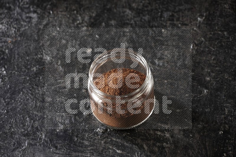 وعاء زجاجي ممتلئ ببودرة القرنفل على أرضية سوداء