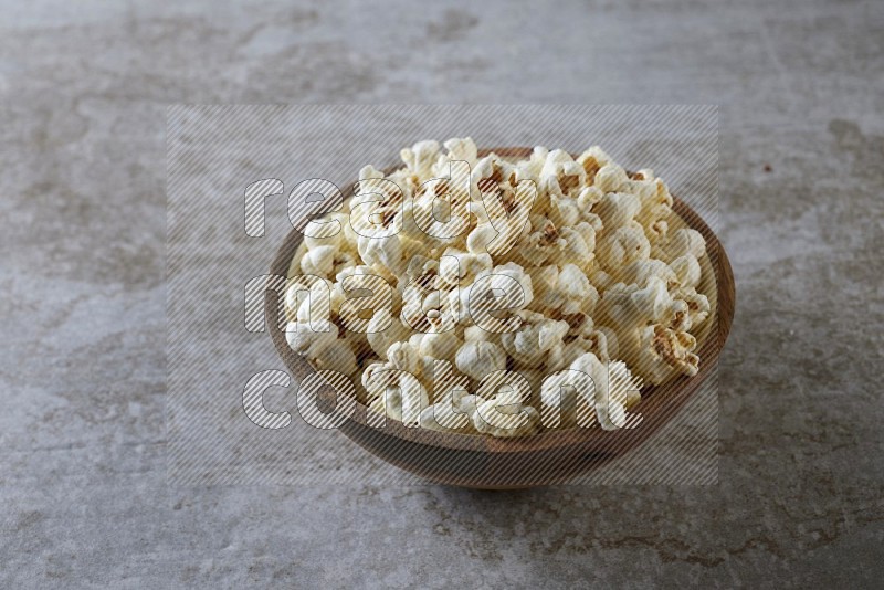 popcorn in wooden bowl on a grey textured countertop