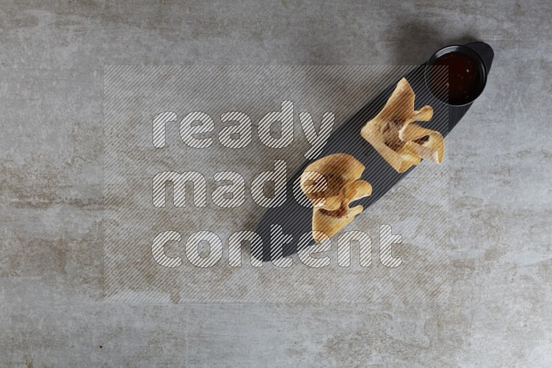 wonton cups with soy sauce ramkin on oval slate on grey textured counter top