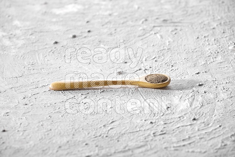 A wooden spoon full of black pepper powder on a textured white flooring