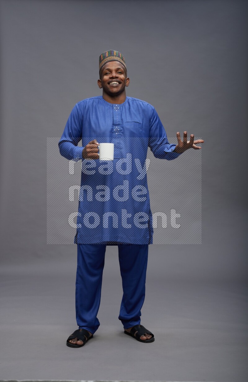 Man wearing Nigerian outfit standing holding mug on gray background