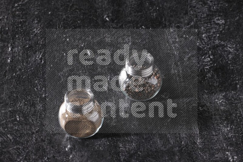 حبوب وبودرة الفلفل الأسود في أوعية زجاجية علي خلفية سوداء