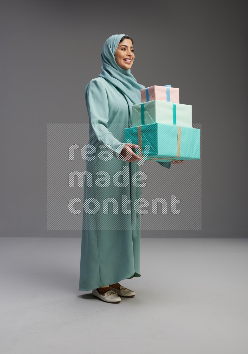 Saudi Woman wearing Abaya standing holding gift box on Gray background