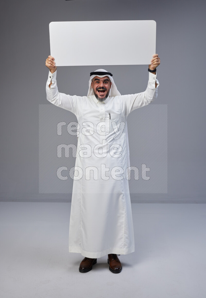 Saudi man Wearing Thob and white Shomag standing holding board on Gray background
