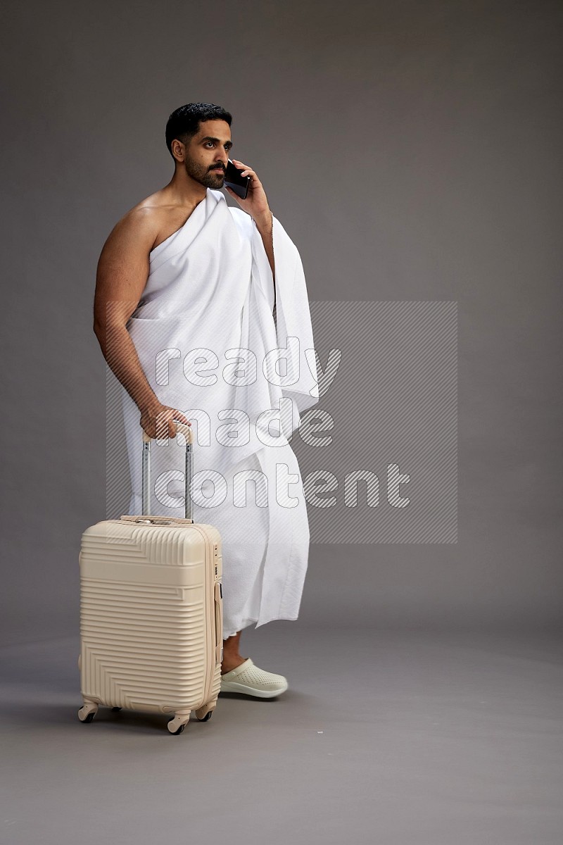 A man wearing Ehram Standing holding traveling bag on gray background