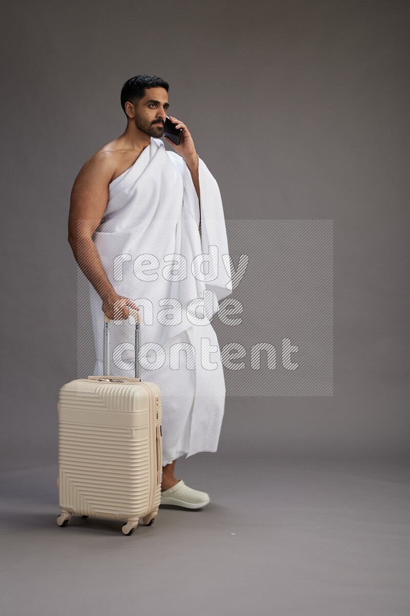 A man wearing Ehram Standing holding traveling bag on gray background