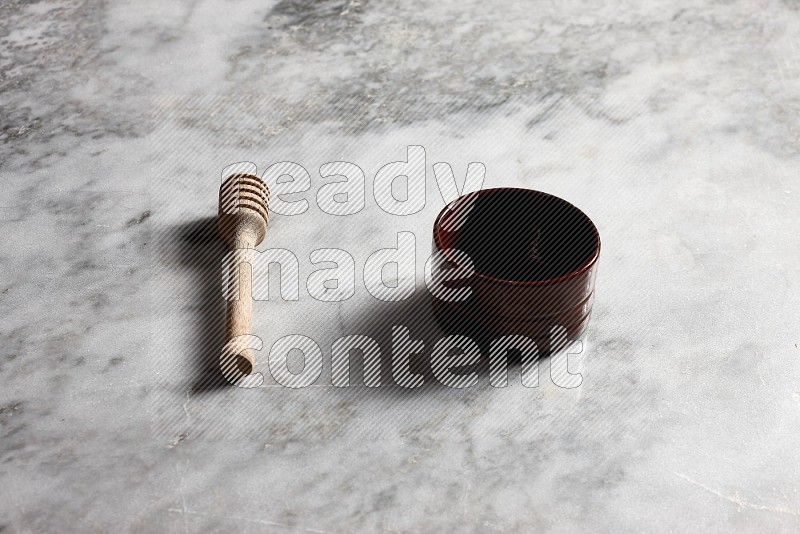 Brown Pottery bowl with wooden honey handle on the side with grey marble flooring, 45 degree angle