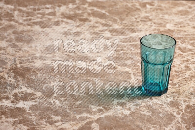A turquoise glass cup on beige marble background