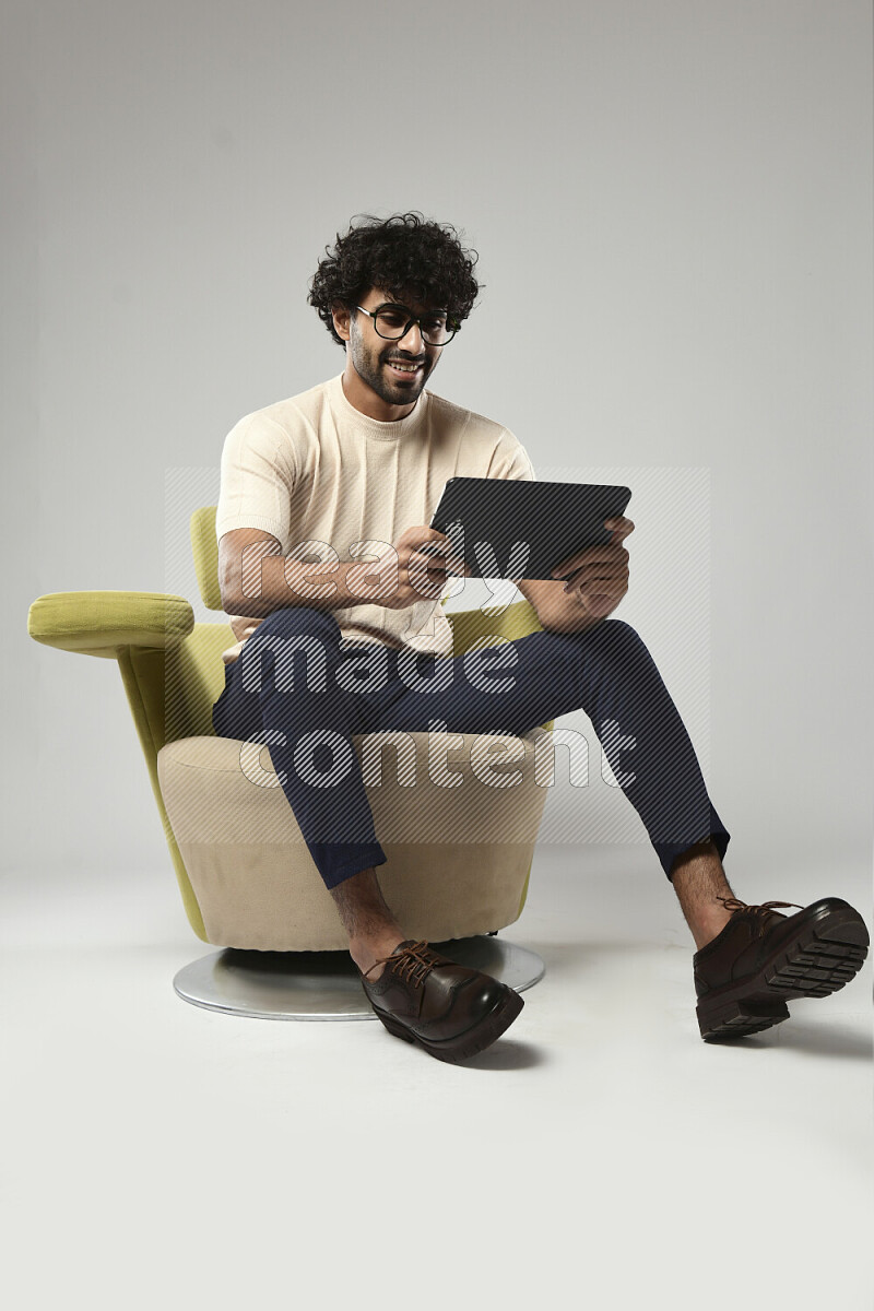 A man wearing casual sitting on a chair gaming on a tablet on white background