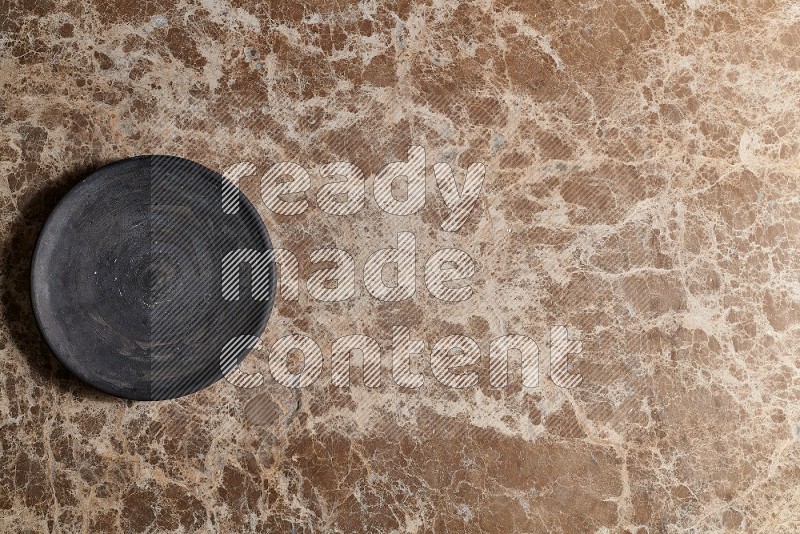 Top View Shot Of A Black Pottery Circular Plate On beige Marble Flooring