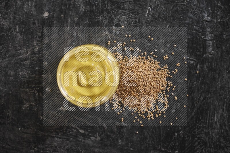 وعاء زجاجي ممتلئ بمعجون الخردل مع بعض بذور الخردل المتناثرة على خلفية سوداء