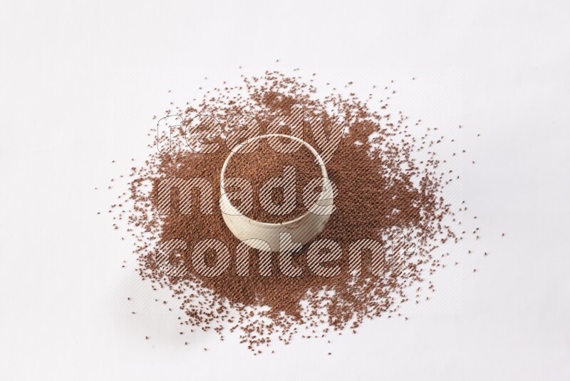 وعاء فخاري بيج ممتلئ ببذور حب الرشاد مع بعض البذور متناثرة على خلفية بيضاء