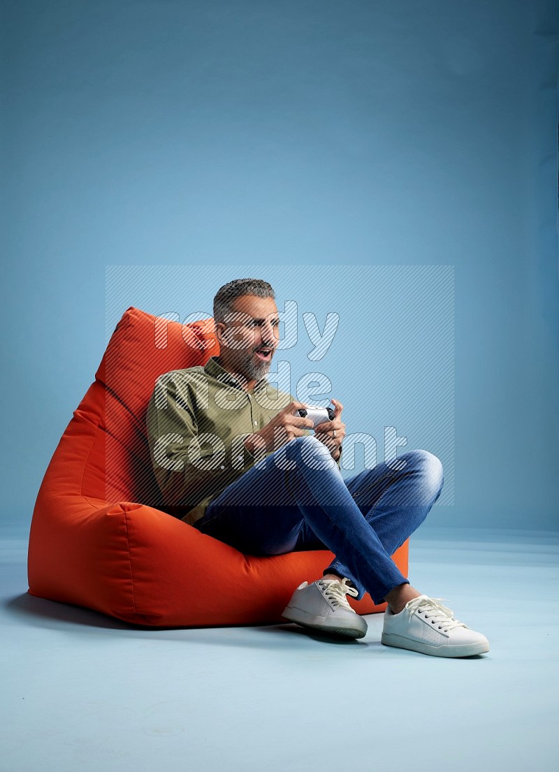 A man sitting on an orange beanbag and gaming with joystick