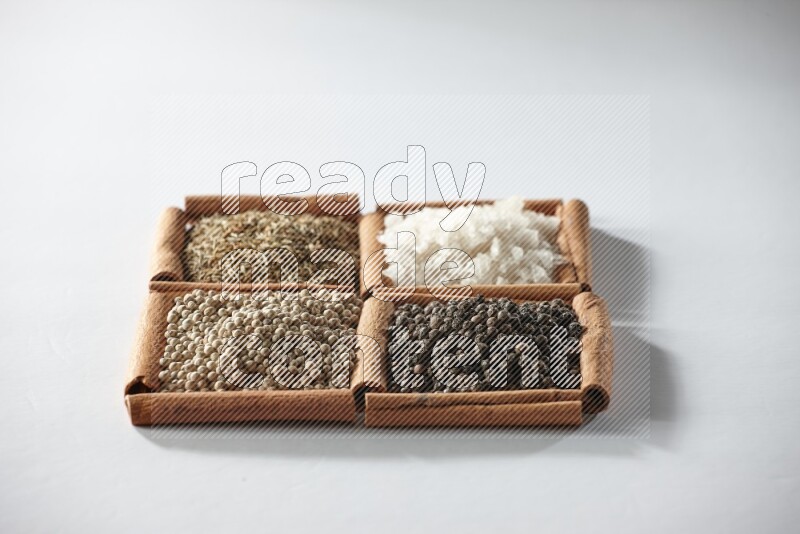 4 مربعات من أعواد القرفة ممتلئة بالكمون والملح والفلفل الأبيض والفلفل الأسود على أرضية بيضاء