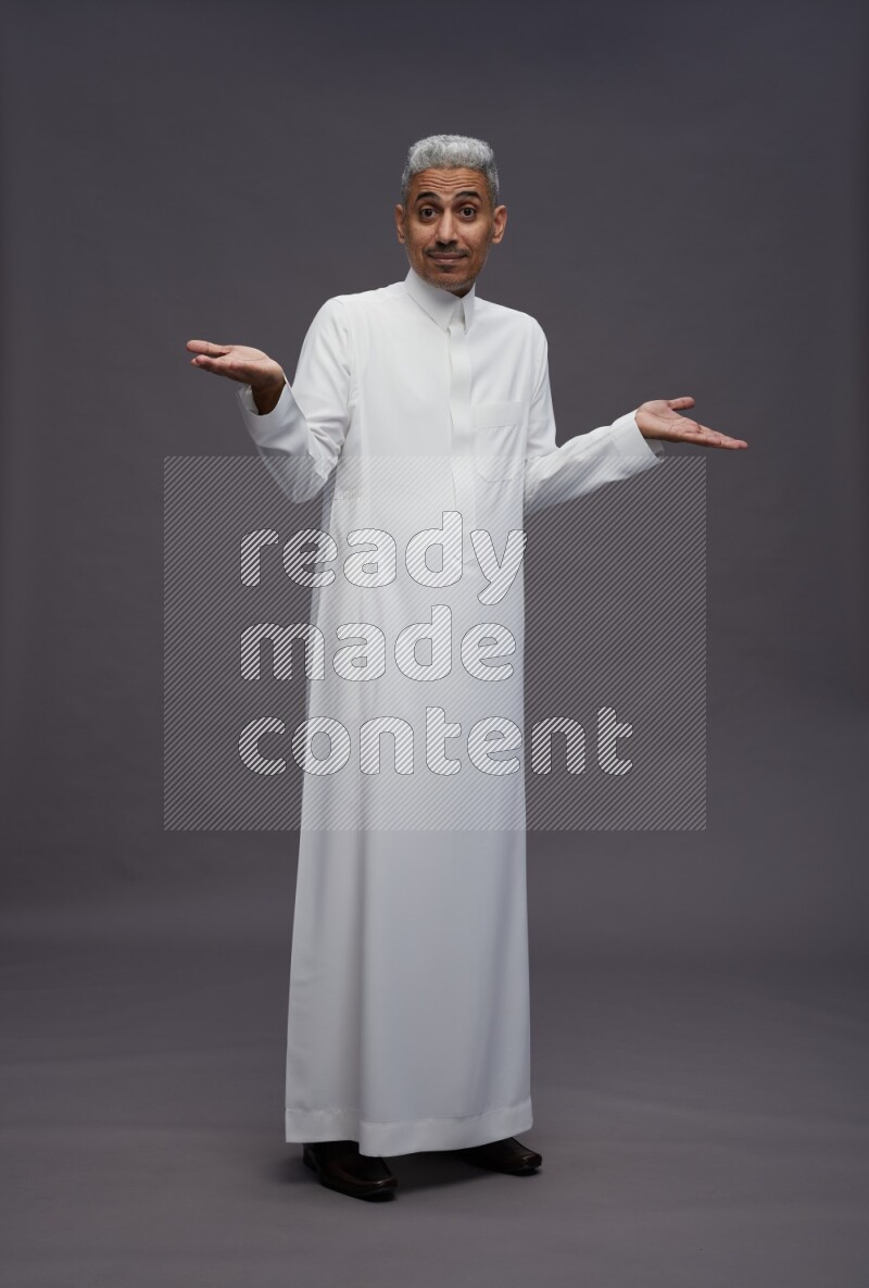Saudi man wearing thob standing interacting with the camera on gray background
