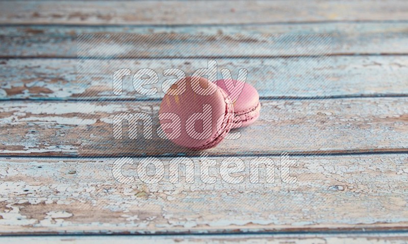 45º Shot of two Purple Strawberry macarons on light blue wooden background