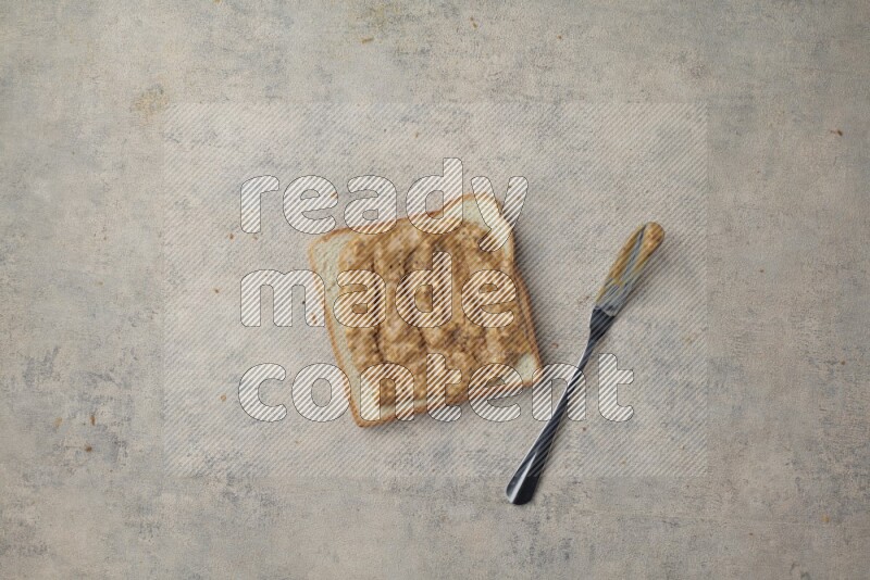 crunchy peanut butter on a white toast with a spreading knife on a light blue textured background
