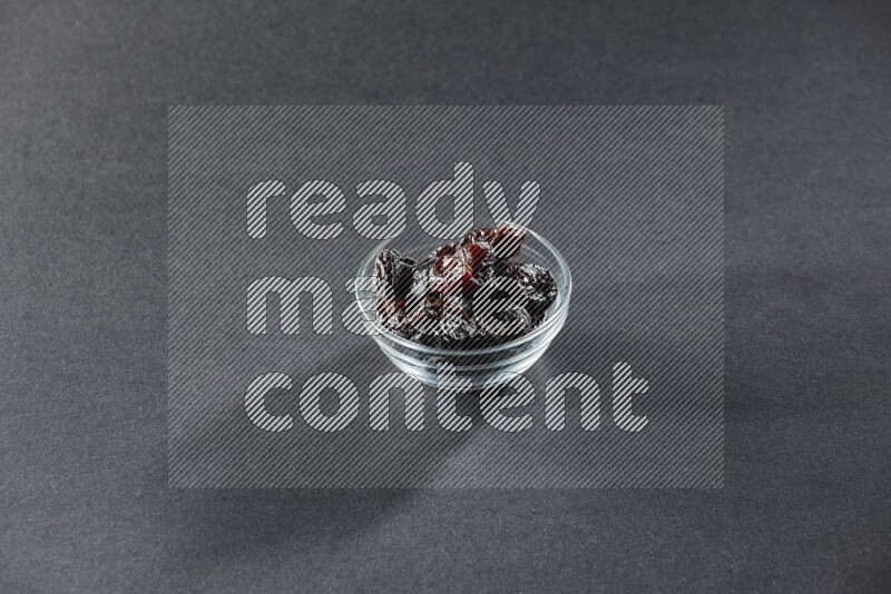 A glass bowl full of dried plums on a black background in different angles