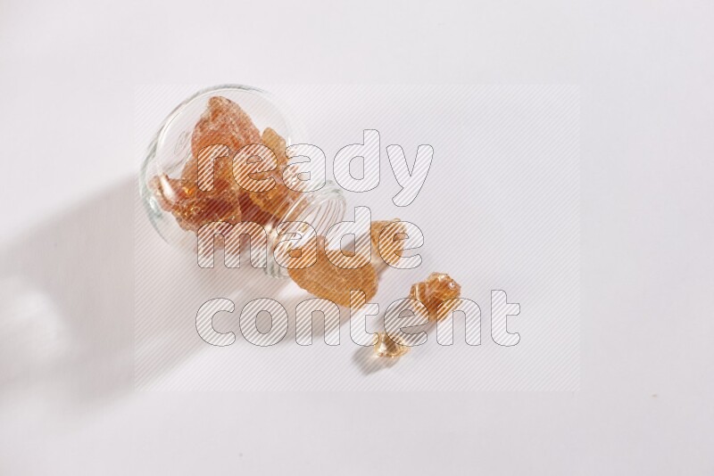 A glass spice jar full of gum arabic and jar is flipped with fallen pieces on white flooring