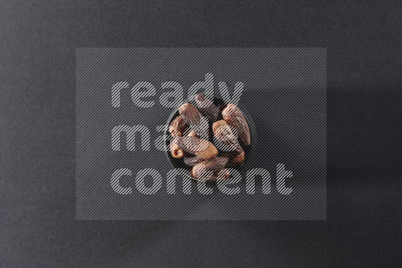 A black pottery bowl full of dried dates on a black background in different angles