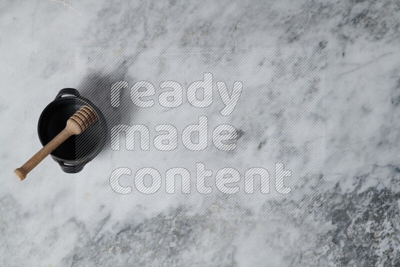 وعاء فخاري أسود مع ملعقة عسل خشبية بداخله على خلفية من الرخام الرمادي