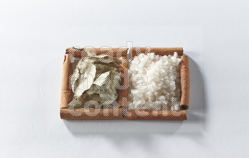 مربعان من أعواد القرفة ممتلئان بالملح الأبيض وأوراق الغار علي خلفية بيضاء