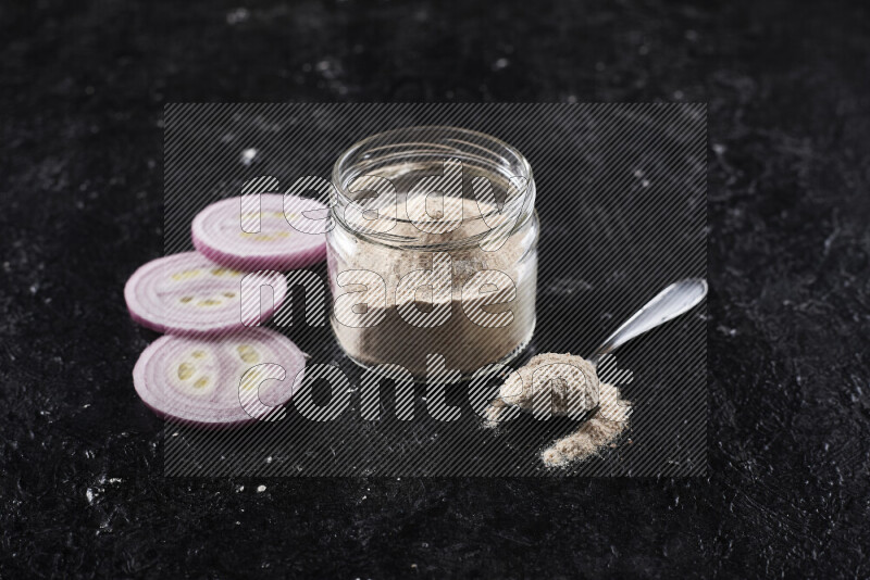 A glass jar full of onion powder on black background