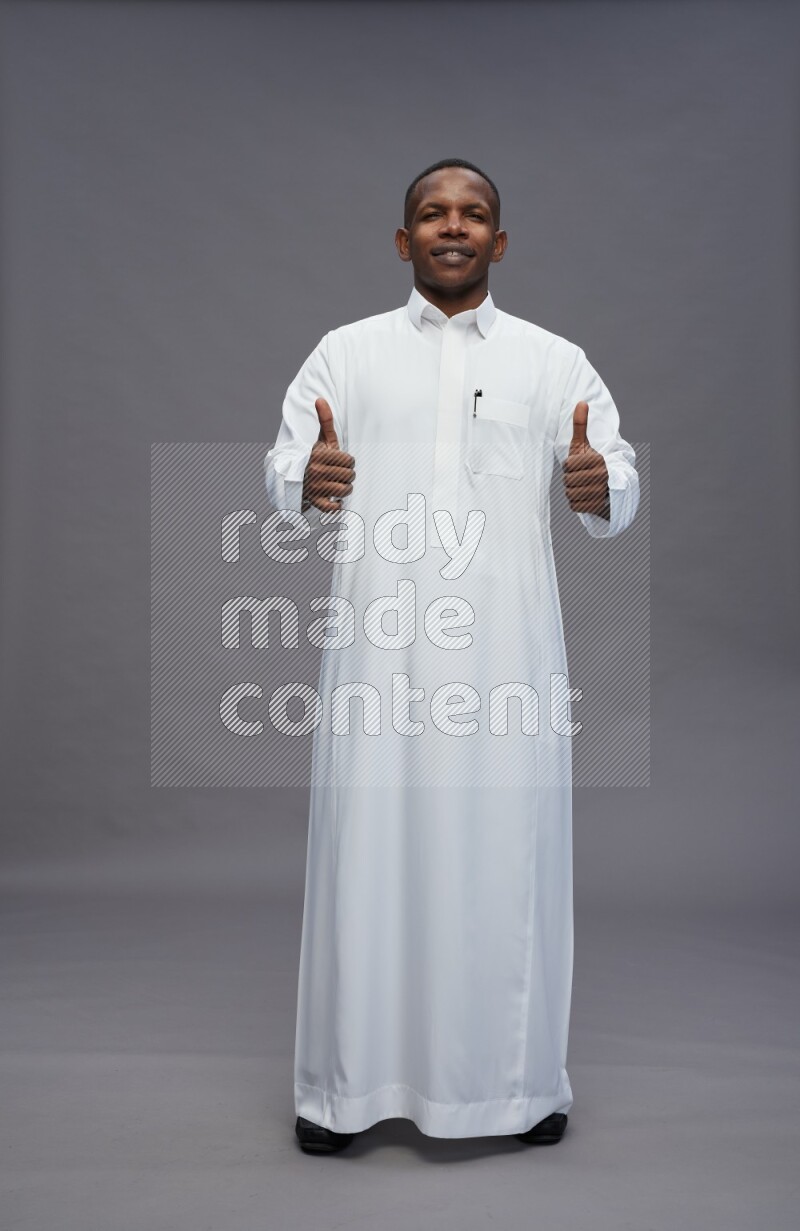 Saudi man wearing thob standing interacting with the camera on gray background