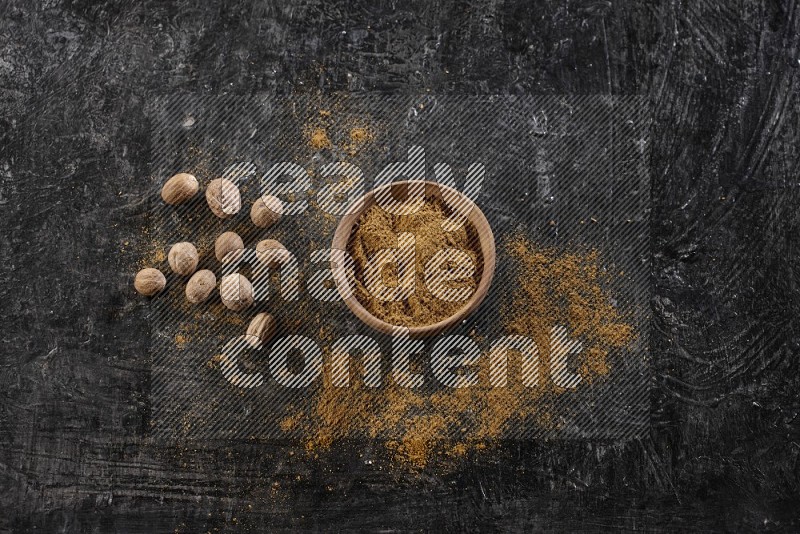 A wooden bowl full of nutmeg powder with the seeds and sprinkled powder beside it on a textured black flooring in different angles