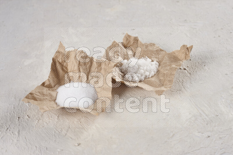 A crumpled piece of paper full of white salt on white background
