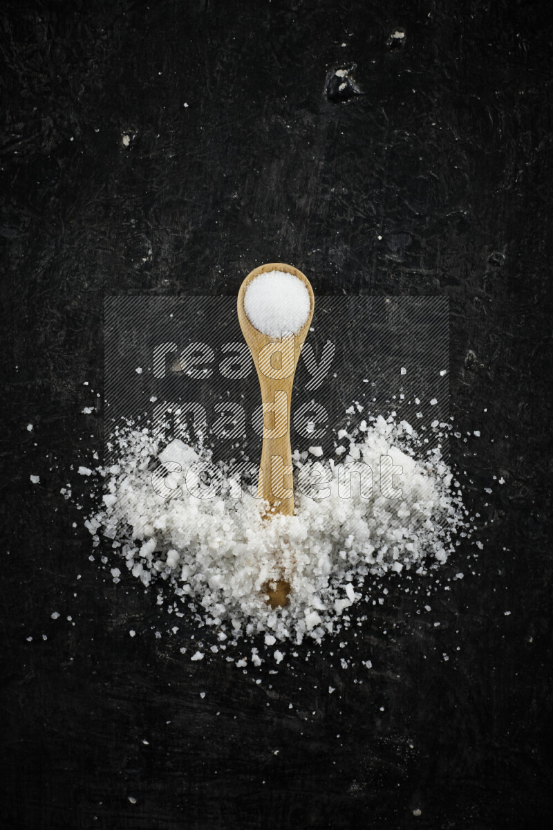 A wooden spoon full of white salt on black background