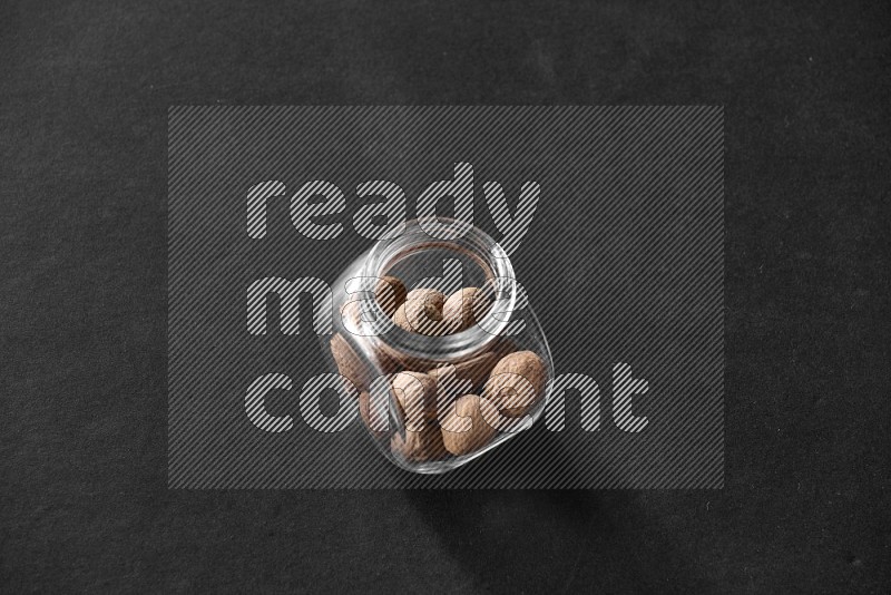 A glass spice jar full of nutmeg on black flooring