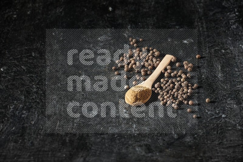 ملاعق خشبية ممتلئة ببودرة بهار الفلفل الحلو وحبوبه بجانبها على خلفية سوداء