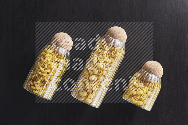 Raw pasta in glass jars on black background