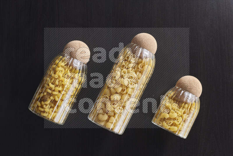 Raw pasta in glass jars on black background
