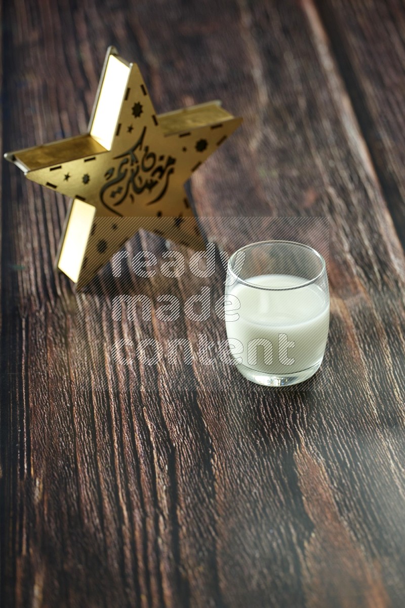 فانوس خشبي نجمي باللون الذهبي مع مشروبات مختلفة وتمر ومكسرات وسبحة صلاة وقرآن على خلفية خشبية بنية