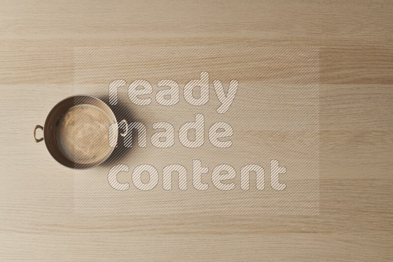 مقلاة نحاسية صغيرة على خلفية خشبية فاتحة