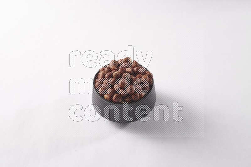 Hazelnuts in a black pottery bowl on white background